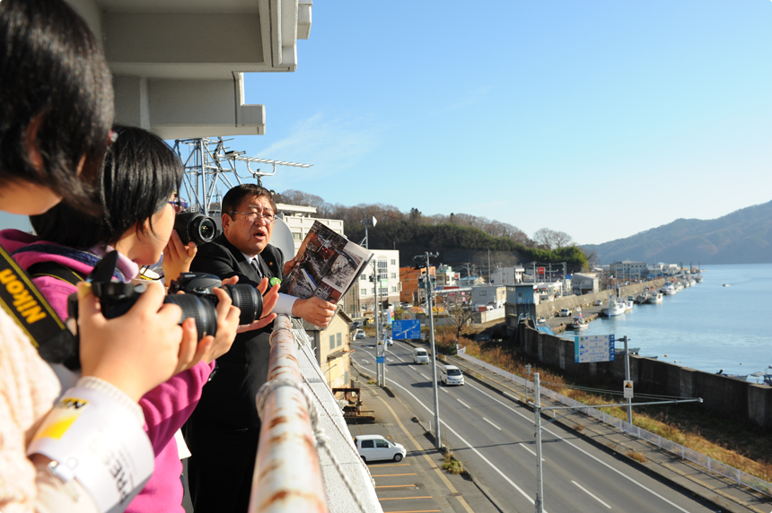 岩手日報の震災写真集を見ながら、津波の様子を語る市長。実際にこの場から、津波が押し寄せるようすが撮影された