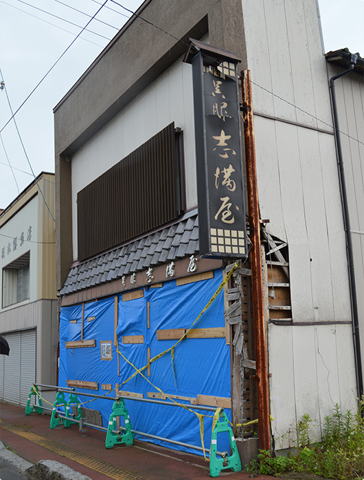 小高地区内の店舗。壁は崩れシートがかけられたままとなっている　－中学生記者 西村くん撮影